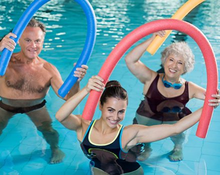 Aqua aerobics with seniors Portrait of smiling people doing aqua fitness together in a swimming pool. Group of senior woman and mature man with swim noodles exercising in a swimming pool. Young trainer and senior people in aqua gym fitness class.